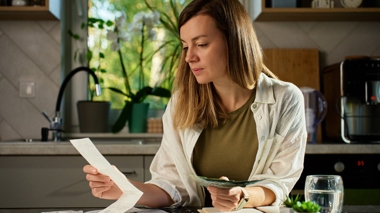 A woman holds her credit card in one hand and her phone in the other, typing in its information to her phone