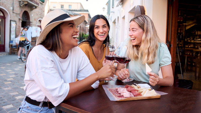 Three happy friends drinking wine and sharing a plate of cured meats and cheeses in Italy