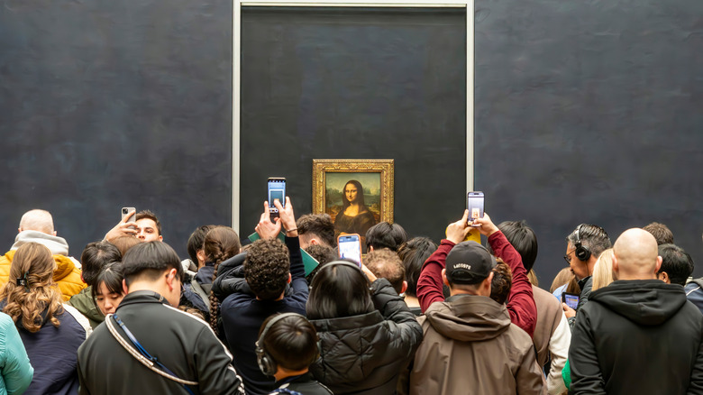 Backs of tourist crowds holding smartphones up to the Mona Lisa