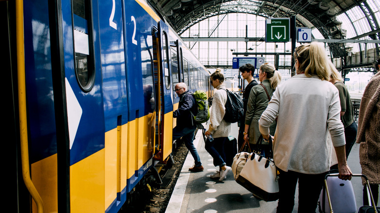 Passengers carrying luggage aboard a blue and yellow train in Amsterdam