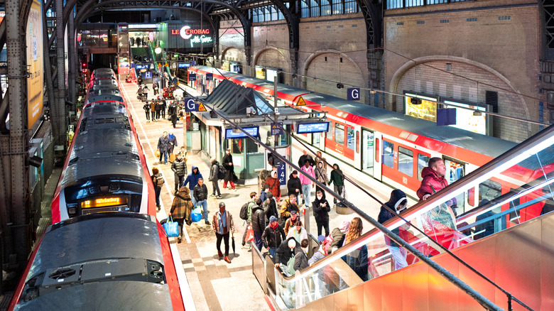 Passengers disembark red Deutsche Bahn trains and ride escalators in Hamburg