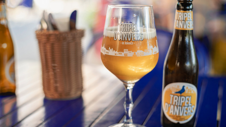 A golden Belgian beer in a glass next to its bottle on a blue table