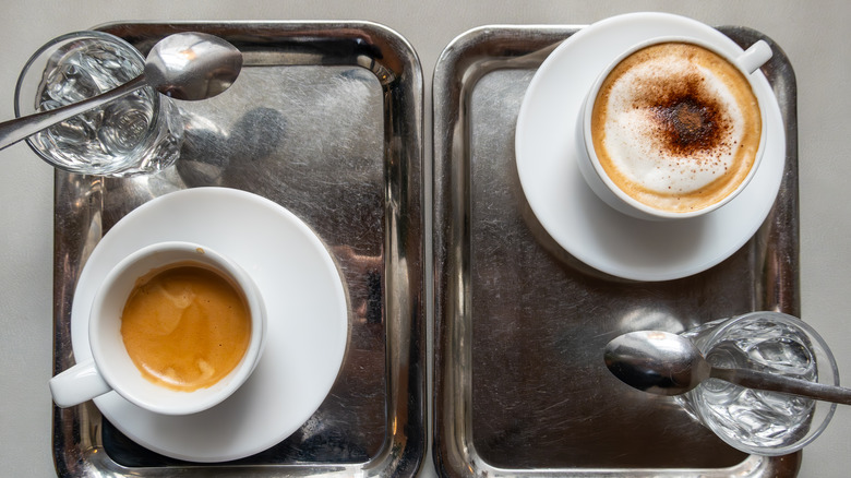 Two coffees on silver trays with water glasses.