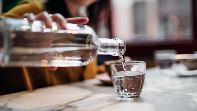 Person pouring a glass bottle of water into a cup.