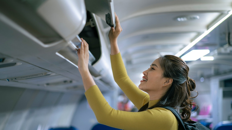 Woman on an airplane and closes the overhead compartment