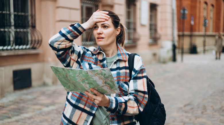 Upset tourist holding a map with her hand on her forehead