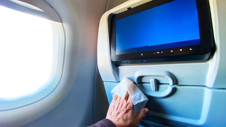 Man using wipes to sanitize his television on the airplane