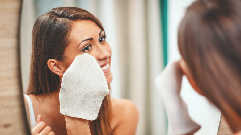 A pretty young woman uses a mitt, an alternative to a washcloth, to clean her face