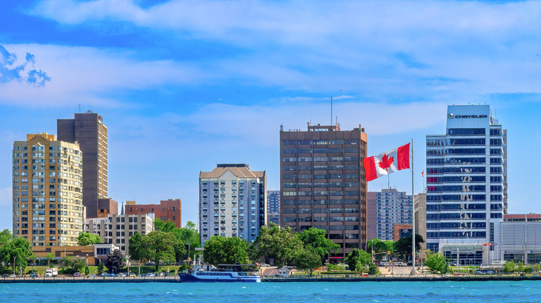 The Windsor skyline and a waving Canadian flag as seen from Detroit with the Detroit River in the foreground