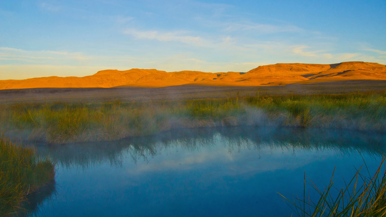 hot springs in shade with sun setting on mountains behind