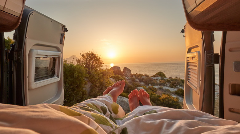 Two people in bed looking at sunrise from camper van