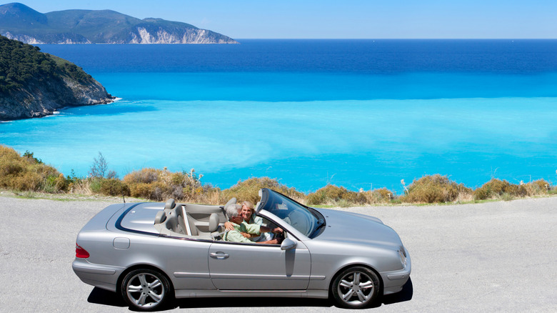 Senior couple driving a coastal road in a convertible car