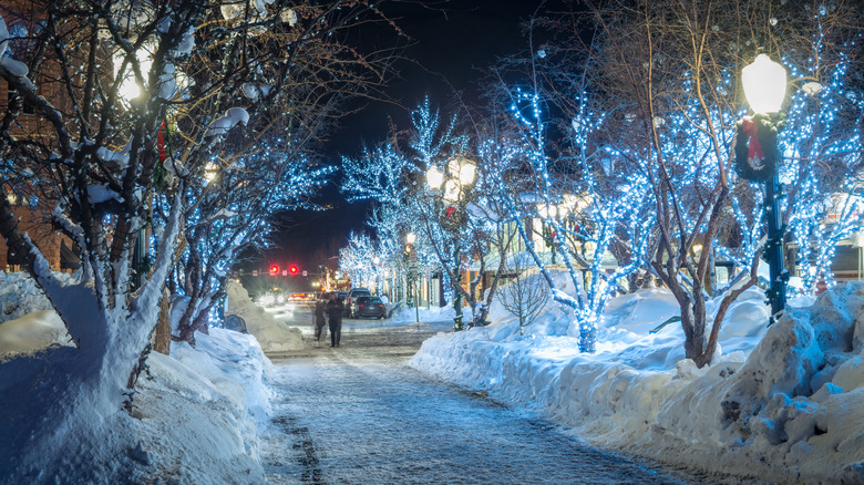 People crossing snowy street with lighted trees in downtown Aspen, Colorado.