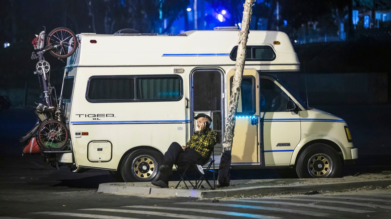 A man sitting outside of his RV at night while parked in a parking lot