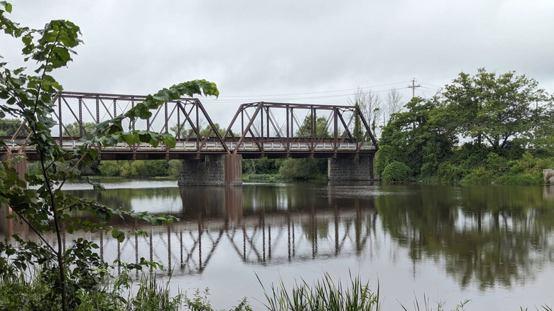 A rusty steel truss bridge crossing the Châteauguay River at Domaine-de-la-Pêche-au-Saumon in Sainte-Martine, Quebec