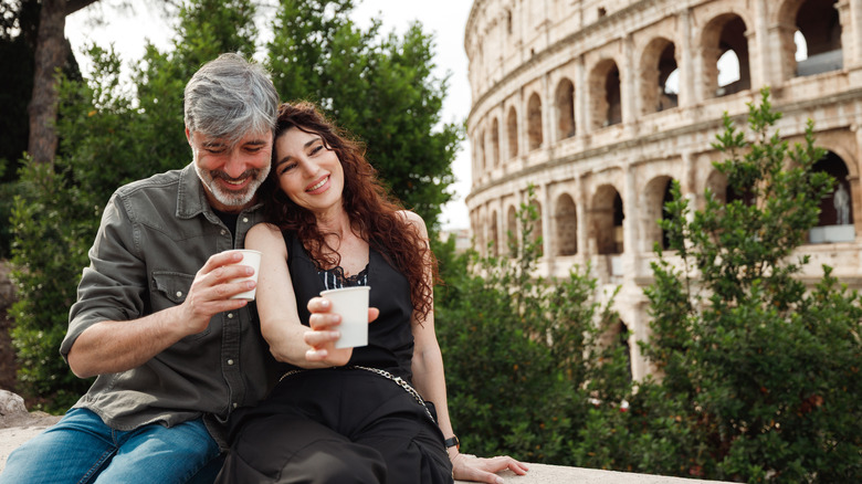 Couple relaxing in Rome, holding paper cups, near the Colosseum