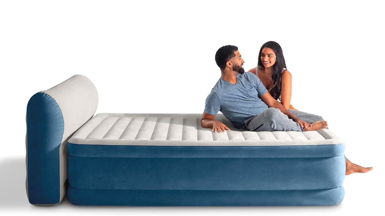 A couple sitting on the end of the Intex DuraBeam Queen Air Mattress against a solid white background.