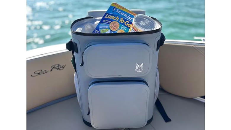 The Member's Mark 24-Can Backpack Cooler sitting open in a boat with snacks visible inside.