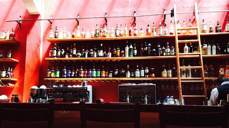 Bottles of liquor line bright colored wall behind bar