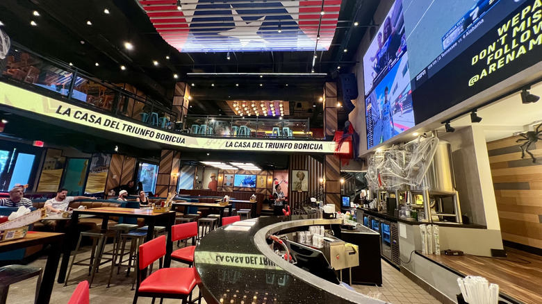 Interior of Arena Medalla, with a bar, tables, chairs, and a second floor, in Isla Grande, Puerto Rico