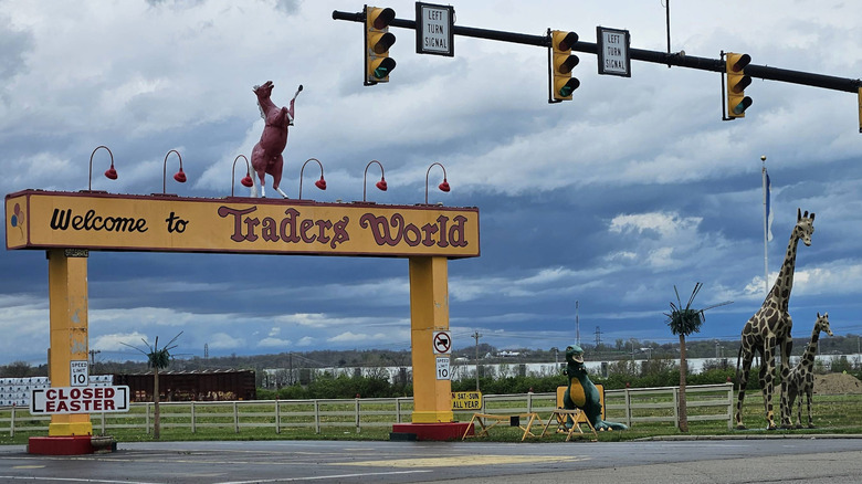 A sign over a road reading "Welcome to Trader's World" in Monroe, Ohio, against a stormy blue sky