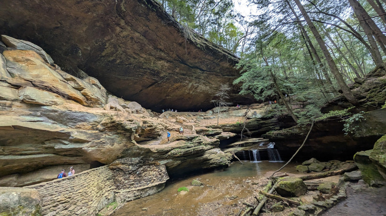 People hiking over large rocks and around a small waterfall in Cooper Hollow Wildlife Area in Oak Hill, Ohio