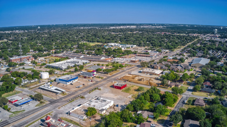 Aerial view of Euless, Texas, showing residential neighborhoods, commercial buildings, tree-lined streets, and development beneath a clear blue sky