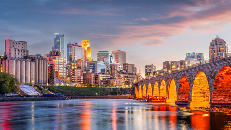 Dusk image of Minneapolis, with skyline lit up and bridge in foreground.