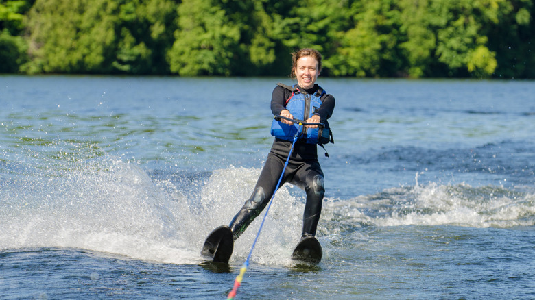 A smiling woman waterskis in a wetsuit