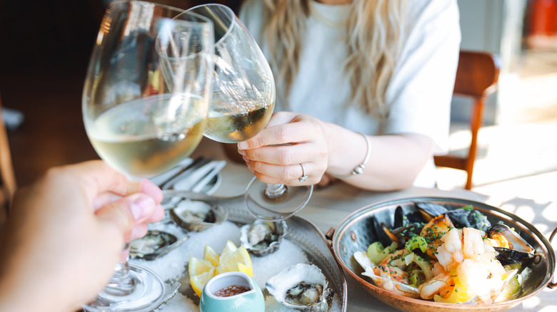 A woman toasts wine glasses at a table spread with seafood at a restaurant.