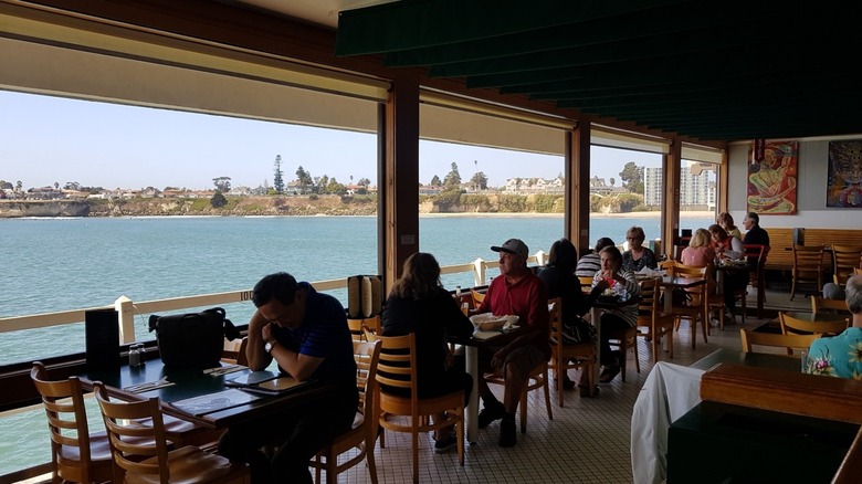 The dining room at Riva Fish House filled with people eating and overlooking the ocean.