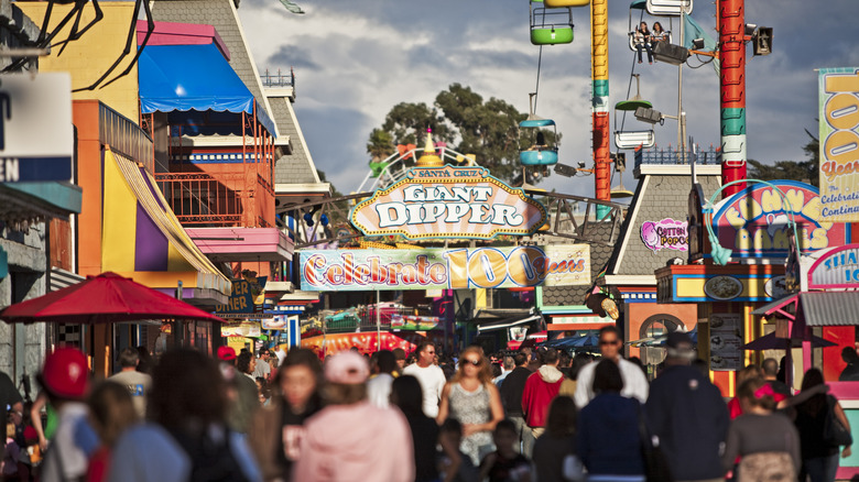 People at the Santa Cruz Beach Boardwalk with rides in the distance