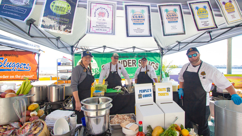 People in aprons standing at a clam chowder booth at the Santa Cruz Clam Chowder Festival