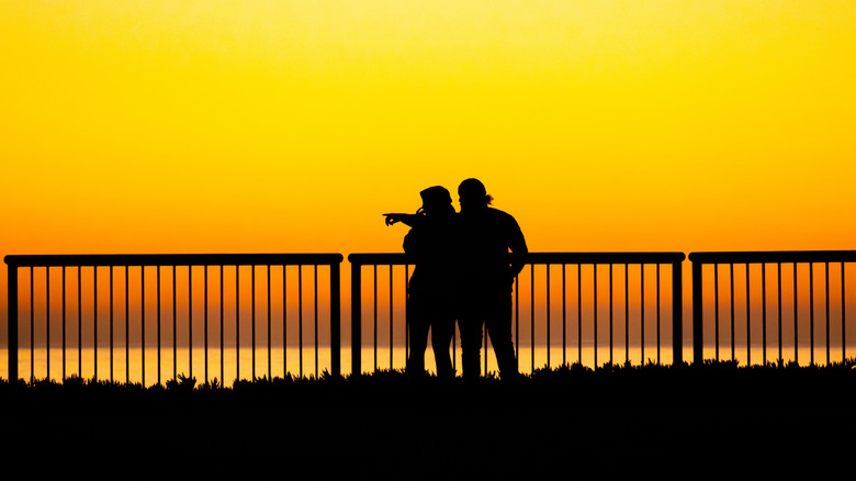 A silhouetted couple watch sunset from the railing in front of Lighthouse Point in Santa Cruz, California.