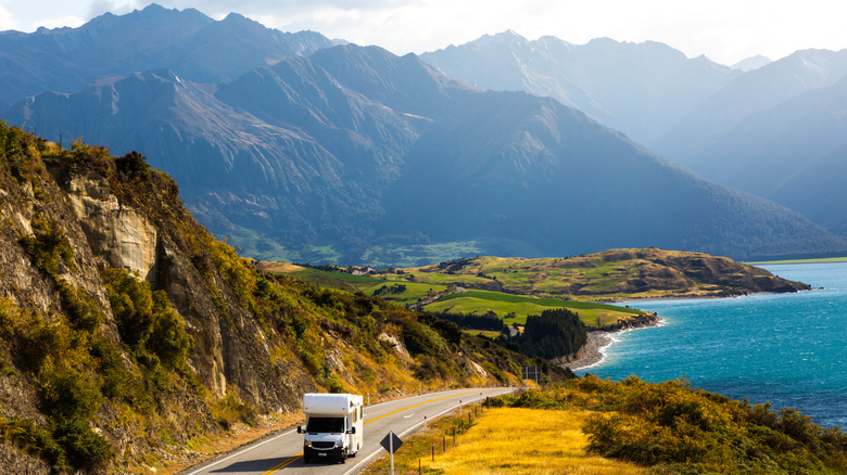 An RV motorhome driving down a road with mountains behind