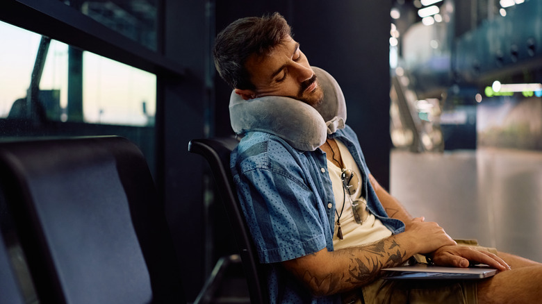 A bulky neck pillow around the head of a man resting at the airport