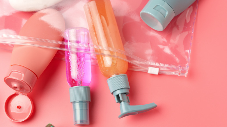 A clear plastic Ziploc bag filled with travel-sized toiletries, set against a pink background