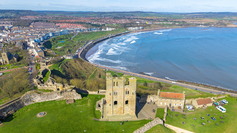 An aerial photo of Scarborough's 3-story castle ruins on a green hilltop with a bay behind it