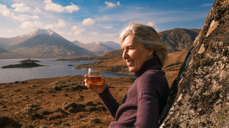 Woman enjoying whisky with Scottish landscape in background