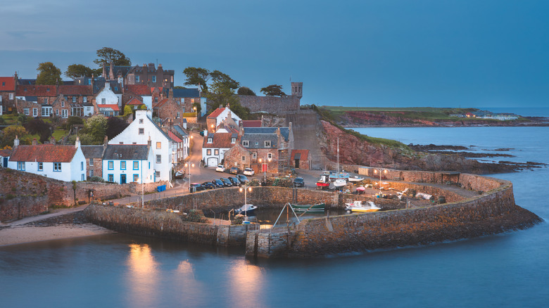 Stone harbor and village houses of Crail set against calm waters at dusk