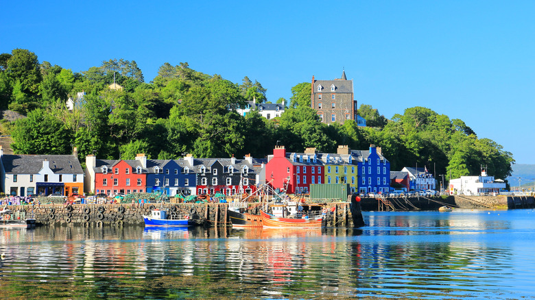 A cluster of colorful buildings against a harbor and greenery under bright blue skies