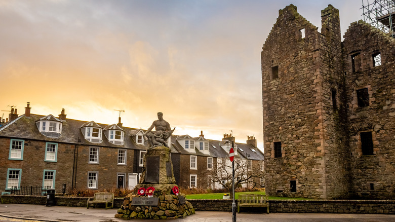 A castle ruin, rows of brick houses, and a statue against a dusky early evening sky