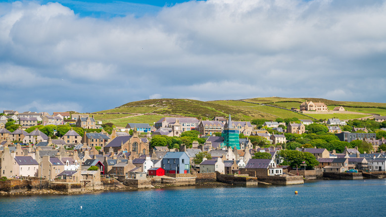 Stromness harbor, a cluster of buildings, and green hills in the backdrop from the water