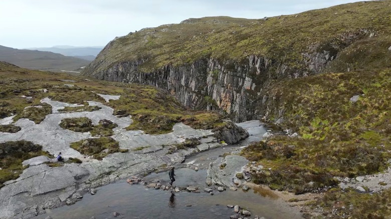 Hiker walking above the Eas a' Chual Aluinn waterfall in Scotland