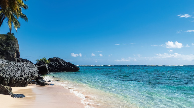 Black rocks and white sand on a beach with crystal blue water