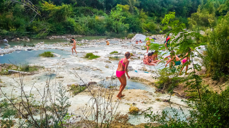 A young woman in pink bathing suit walks to a hot spring with other visitors