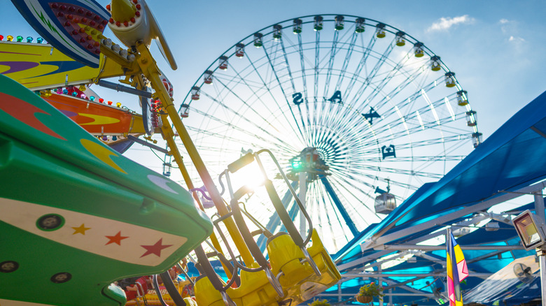 Rides and a Ferris wheel crowd together in a landscape backlit by a bright sun