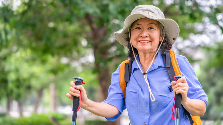 A happy senior woman with a backpack and trekking poles hikes through a national park.