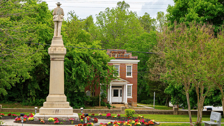 red brick building underneath blue sky and green trees with statue in foreground
