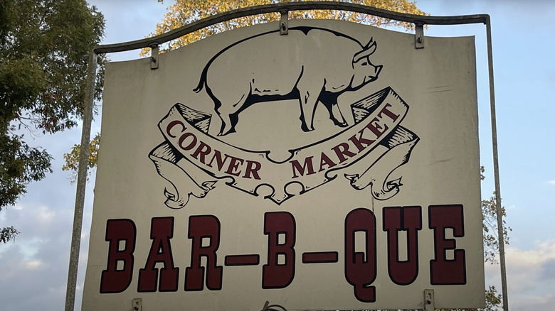 white sign with red text and a drawing of a pig in front of blue sky
